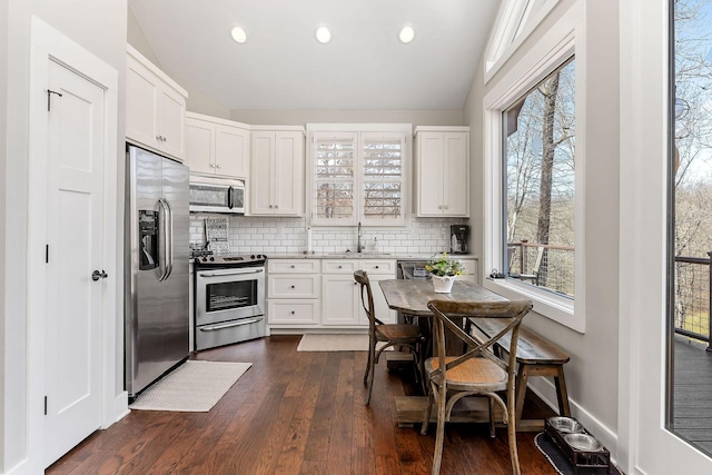 kitchen with dark wood-style flooring, stainless steel appliances, backsplash, white cabinetry, and baseboards