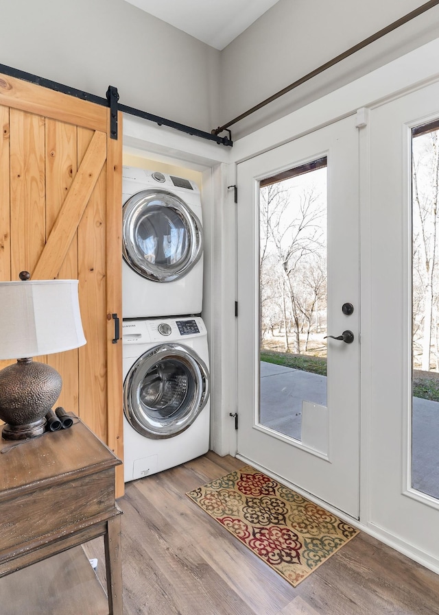 washroom featuring laundry area, a barn door, stacked washer / dryer, and wood finished floors