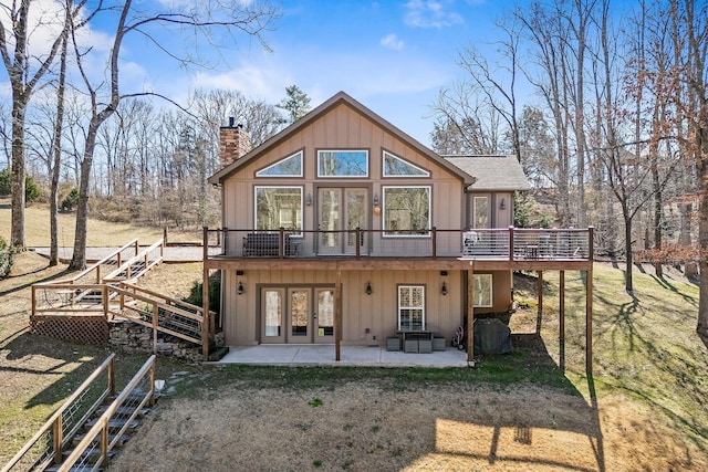 back of property featuring a deck, a patio, a shingled roof, french doors, and a chimney