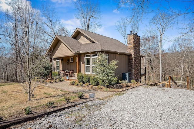 craftsman-style home with a chimney, covered porch, central AC unit, board and batten siding, and driveway