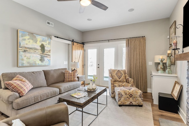 living area featuring a barn door, light wood-type flooring, a ceiling fan, and baseboards