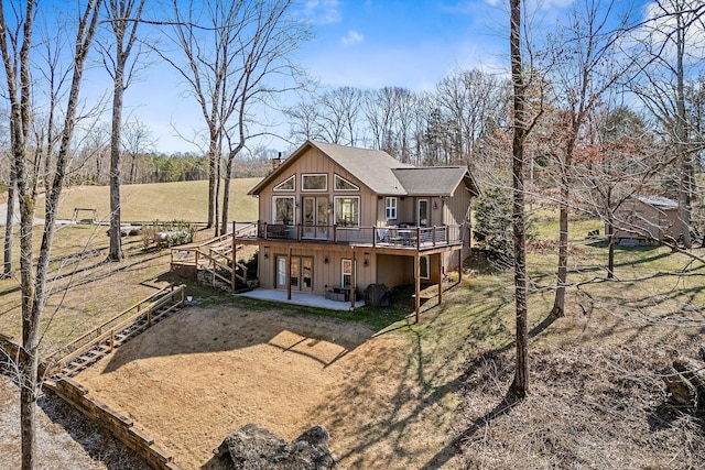 rear view of house with driveway, a wooden deck, roof with shingles, and a patio