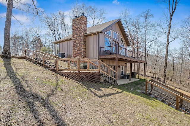 rear view of property with roof with shingles, a chimney, board and batten siding, a patio area, and a deck