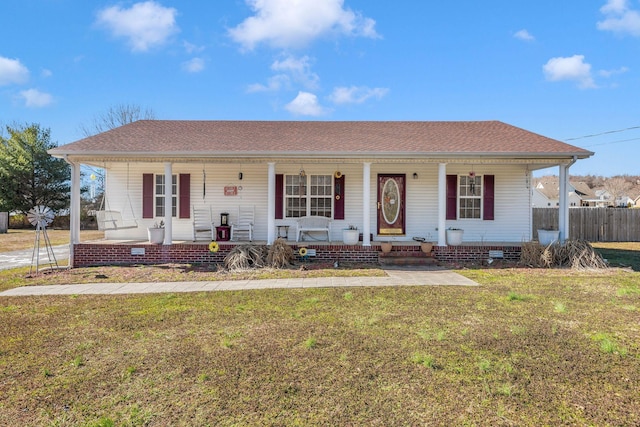 view of front facade with a shingled roof, a front yard, covered porch, and fence