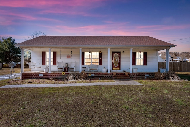 view of front of house with covered porch, roof with shingles, fence, and a front yard