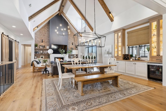 dining room featuring a large fireplace, a barn door, light wood-style flooring, wine cooler, and beam ceiling