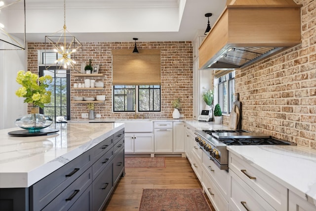 kitchen with brick wall, custom range hood, gray cabinets, open shelves, and stainless steel gas stovetop