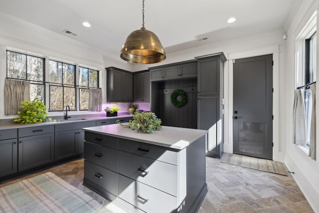 kitchen featuring a sink, visible vents, hanging light fixtures, stone finish floor, and crown molding