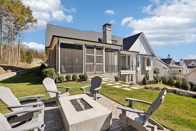 rear view of property with a yard, a patio, a chimney, an outdoor fire pit, and a sunroom