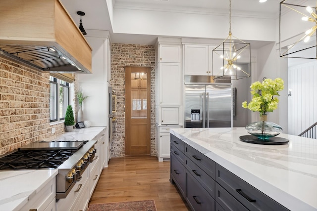 kitchen with white cabinets, brick wall, light wood-style flooring, custom exhaust hood, and stainless steel appliances