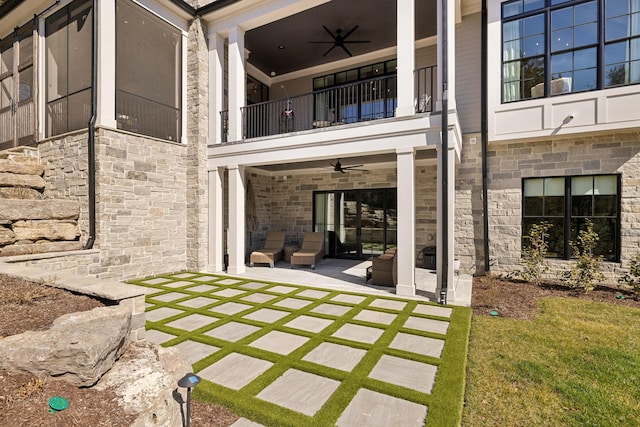 back of property featuring ceiling fan, a patio, stone siding, and a balcony