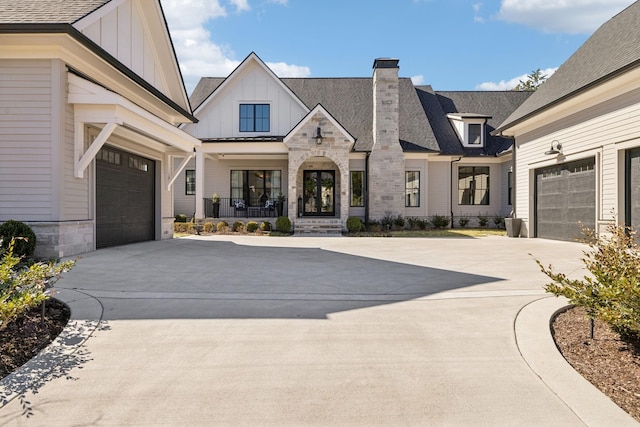 view of front of property featuring a garage, driveway, stone siding, board and batten siding, and a chimney