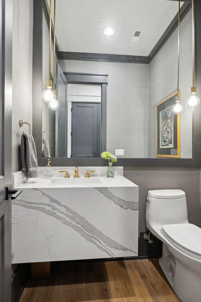 half bath featuring toilet, wood finished floors, vanity, visible vents, and crown molding