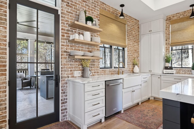 kitchen with open shelves, stainless steel dishwasher, white cabinetry, a sink, and brick wall