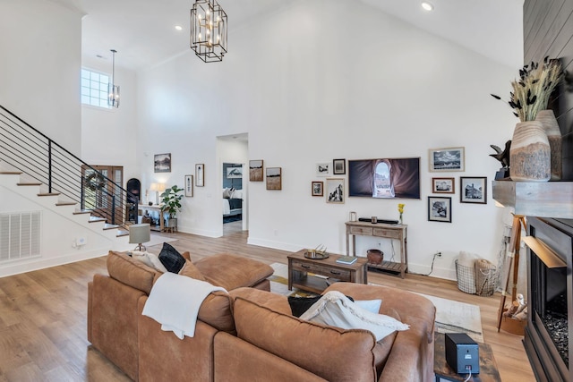 living room with visible vents, wood finished floors, stairs, a fireplace, and a notable chandelier