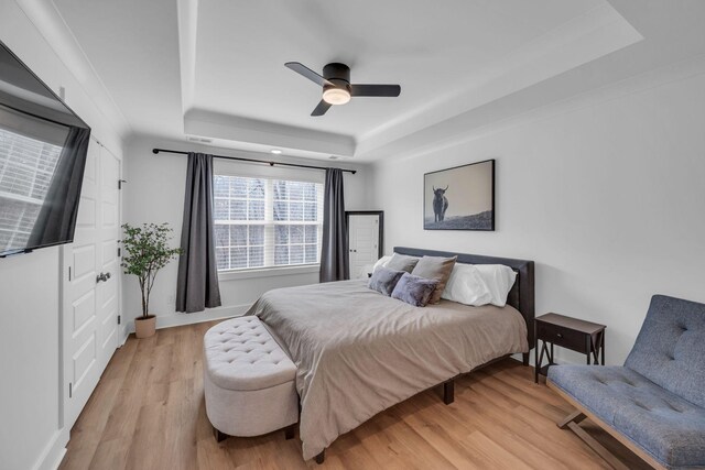 bedroom with light wood-type flooring, ceiling fan, and a raised ceiling