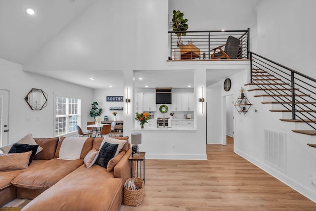 living area featuring light wood finished floors, visible vents, a towering ceiling, stairway, and baseboards