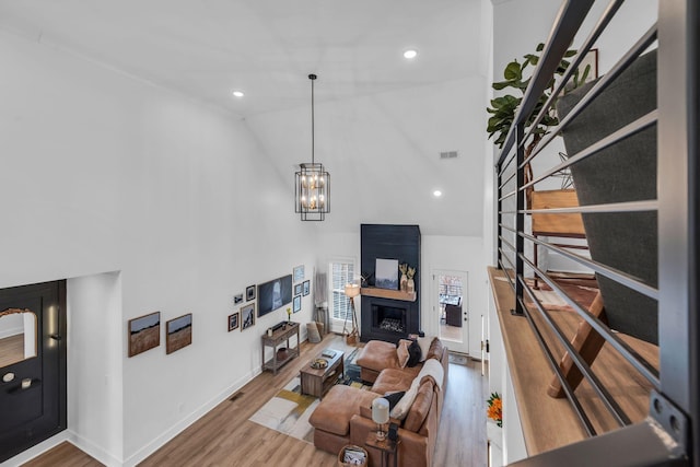 living area featuring a fireplace, a notable chandelier, visible vents, wood finished floors, and high vaulted ceiling