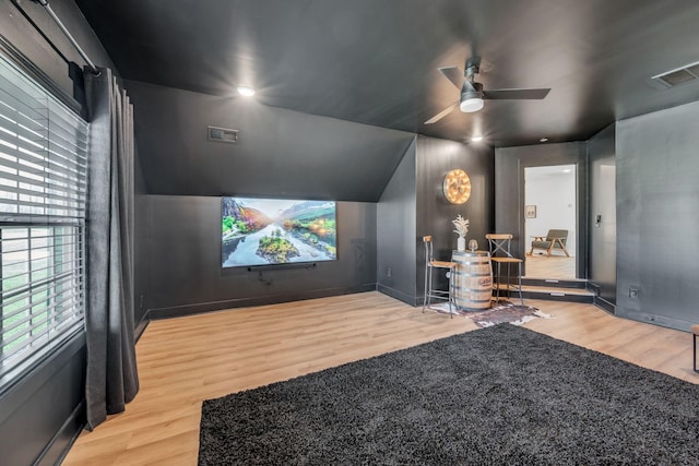 home theater featuring lofted ceiling, ceiling fan, wood finished floors, and visible vents