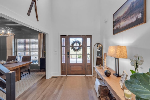 entrance foyer with visible vents, a towering ceiling, light wood finished floors, and an inviting chandelier