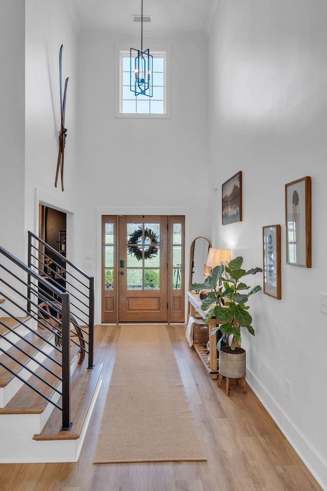 foyer entrance featuring wood finished floors, visible vents, baseboards, stairs, and crown molding