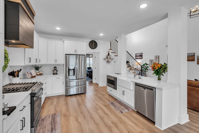 kitchen with stainless steel appliances, wall chimney exhaust hood, a sink, and light wood-style flooring