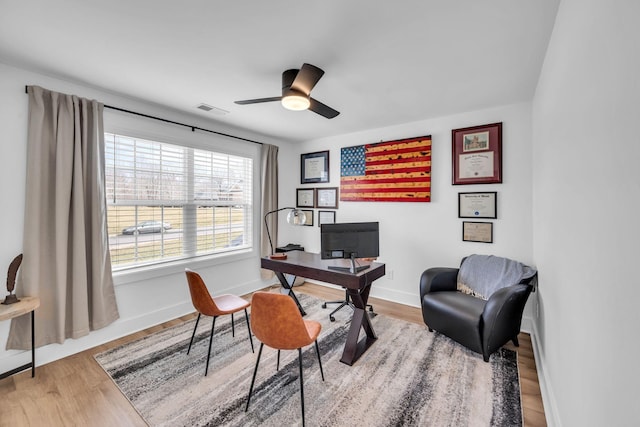 home office with a ceiling fan, wood finished floors, visible vents, and baseboards