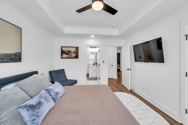 bedroom with ornamental molding, a raised ceiling, baseboards, and wood finished floors