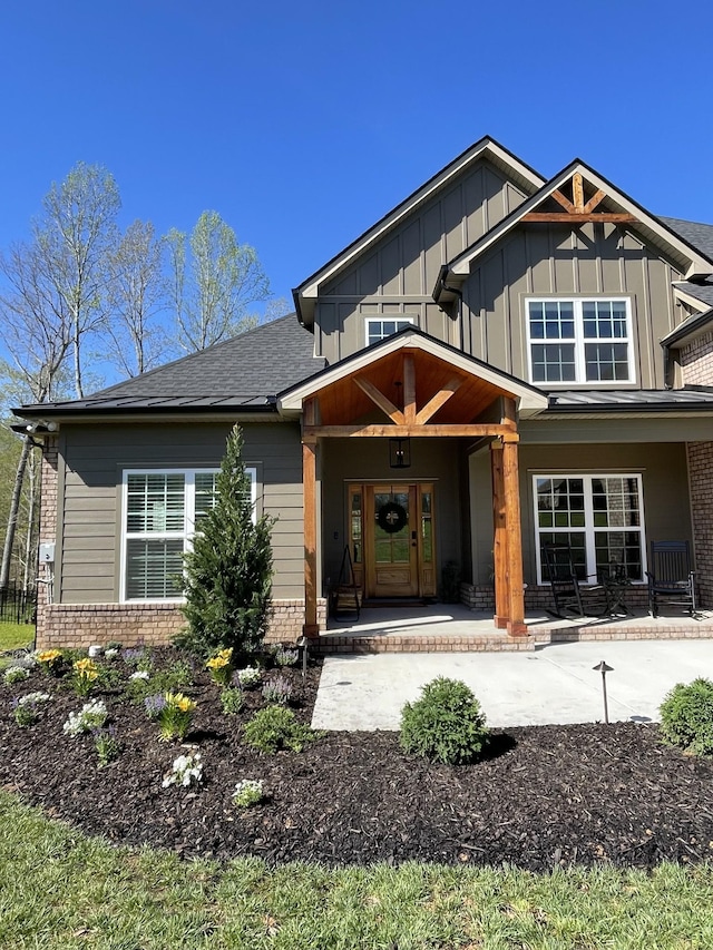 view of front of house featuring board and batten siding, brick siding, a porch, and roof with shingles