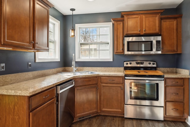 kitchen featuring stainless steel appliances, a sink, dark wood-style floors, brown cabinetry, and pendant lighting