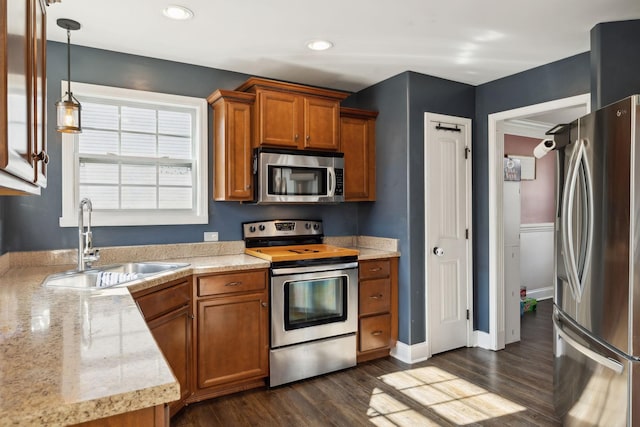 kitchen featuring stainless steel appliances, brown cabinetry, a sink, and dark wood-style floors