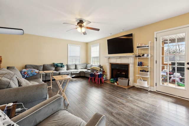 living room featuring a ceiling fan, a fireplace with raised hearth, and wood finished floors