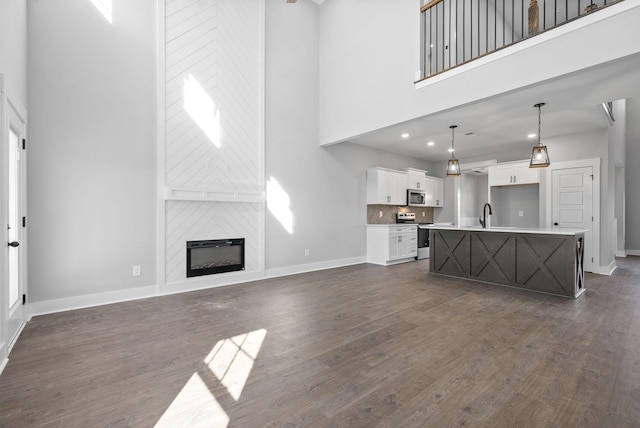 living room featuring a fireplace, recessed lighting, a high ceiling, dark wood-type flooring, and baseboards