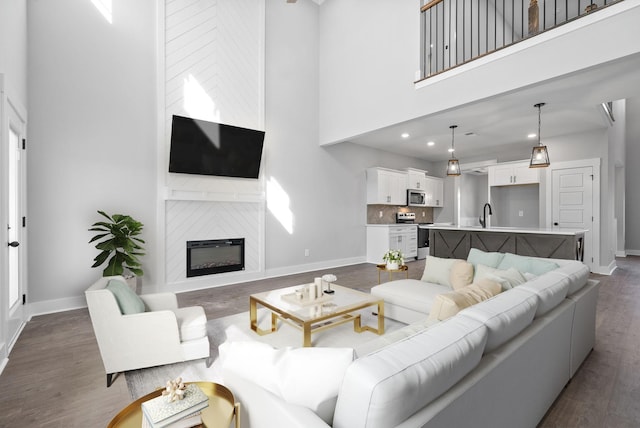 living area with a large fireplace, a high ceiling, baseboards, and dark wood-style flooring