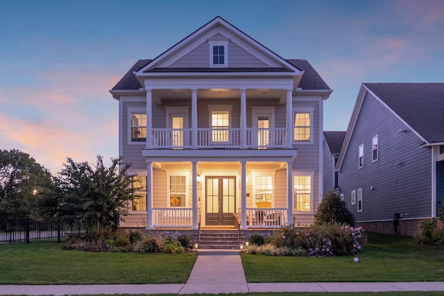 view of front of house with a balcony, fence, a porch, and a lawn