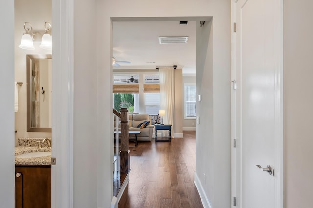 hall featuring dark wood-style flooring, visible vents, a sink, and baseboards