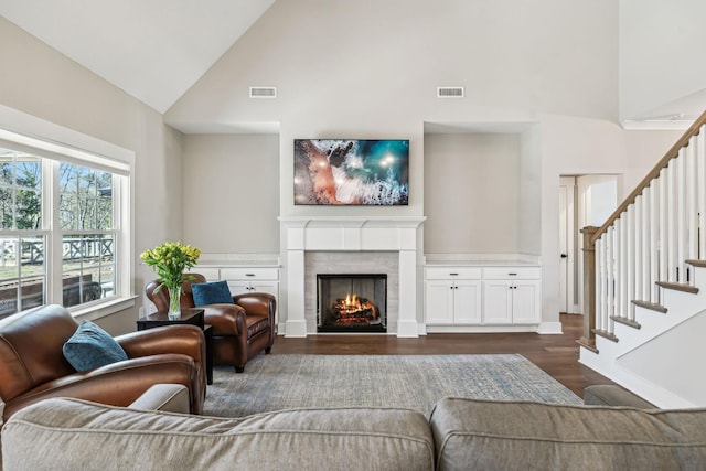 living area featuring dark wood-type flooring, visible vents, a fireplace, and stairs