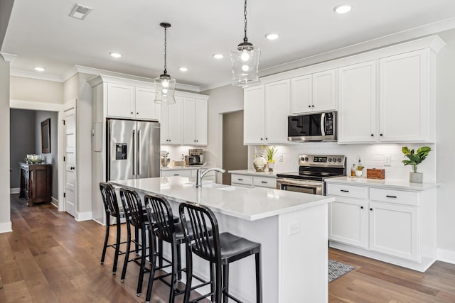 kitchen with a kitchen island with sink, visible vents, appliances with stainless steel finishes, dark wood-style floors, and tasteful backsplash