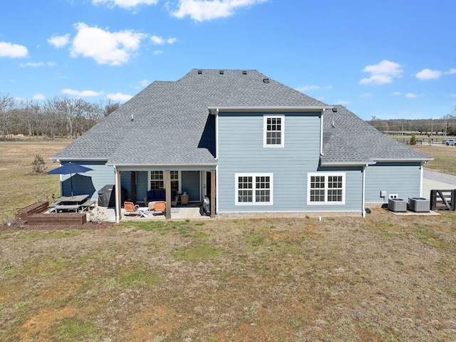 rear view of property featuring a patio area, a shingled roof, central AC, and a yard