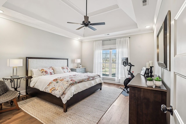 bedroom featuring a tray ceiling, visible vents, ceiling fan, and wood finished floors