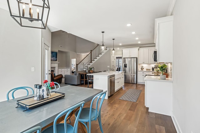 kitchen featuring dark wood finished floors, appliances with stainless steel finishes, a kitchen island with sink, light countertops, and white cabinetry