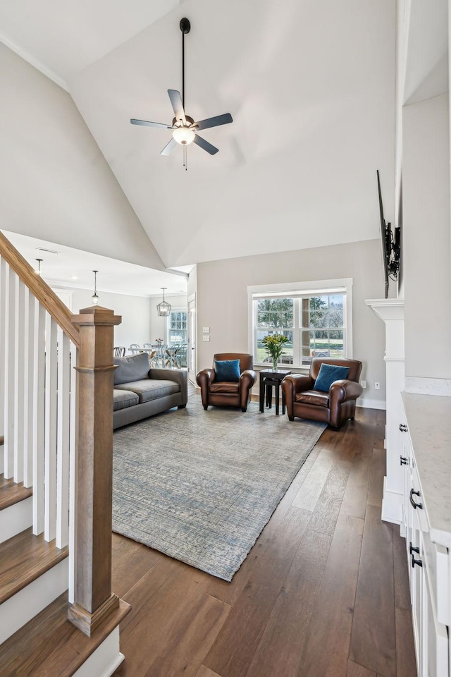 living area with dark wood-style flooring, a fireplace, stairway, a ceiling fan, and high vaulted ceiling