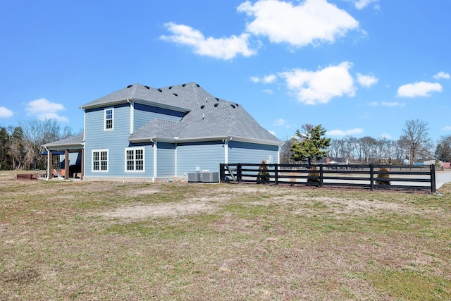 rear view of property with roof with shingles, a lawn, and fence