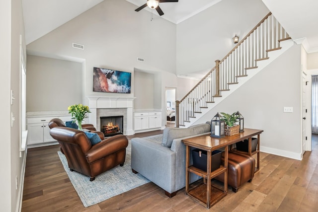 living area with a warm lit fireplace, wood finished floors, visible vents, and baseboards