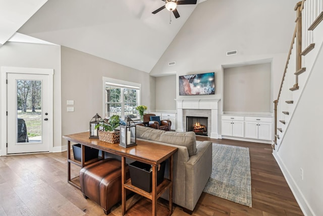 living area featuring visible vents, baseboards, dark wood-style floors, a lit fireplace, and high vaulted ceiling