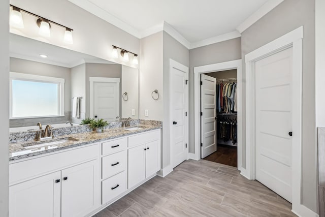 full bathroom featuring double vanity, crown molding, a spacious closet, and a sink