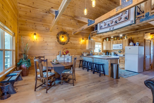 dining room featuring light wood-style flooring, beamed ceiling, and wooden walls