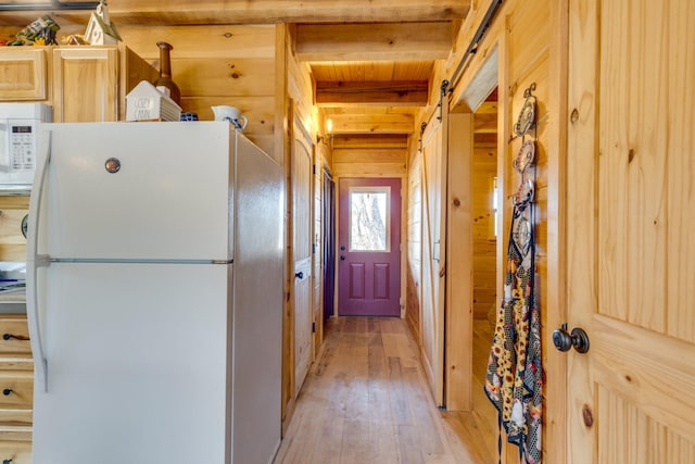 kitchen with beam ceiling, a barn door, light wood-style floors, wood walls, and white appliances