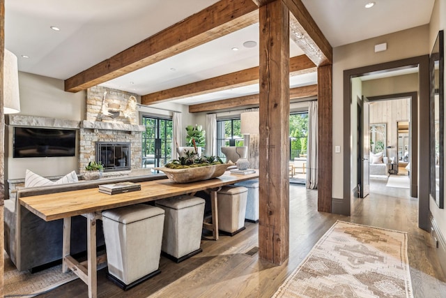 kitchen featuring open floor plan, wood finished floors, beamed ceiling, a stone fireplace, and wooden counters