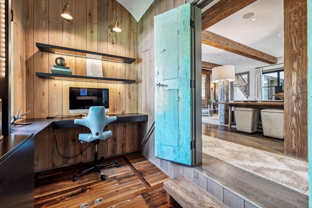 office area with beam ceiling, wood walls, built in desk, and hardwood / wood-style floors